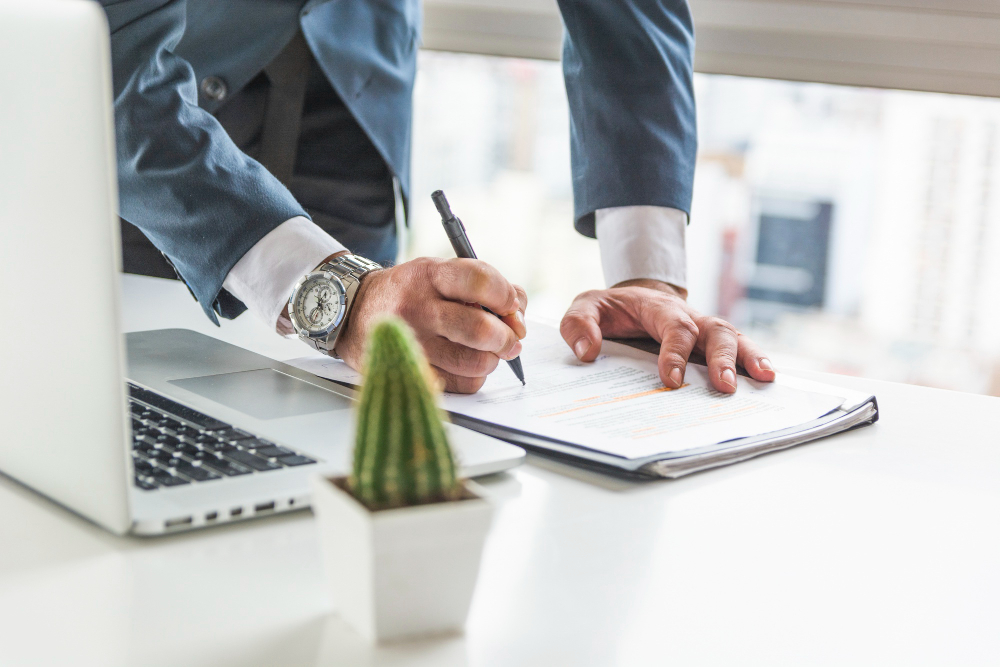 businessman-writing-document-with-pen-desk-with-laptop